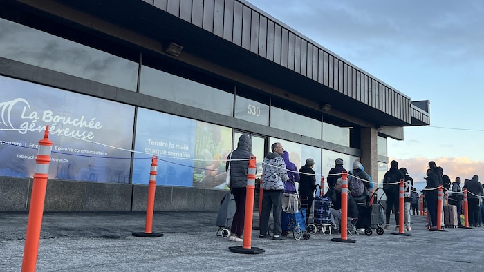 Des gens font la file à l'extérieur du bâtiment d'une banque alimentaire.