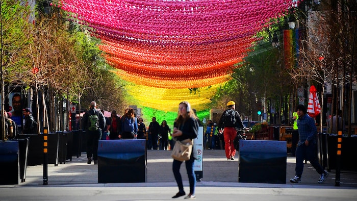 Des gens marchent sur la rue Sainte-Catherine. Au-dessus d'eux sont installées des milliers de boules de toutes les couleurs de l'arc-en-ciel.