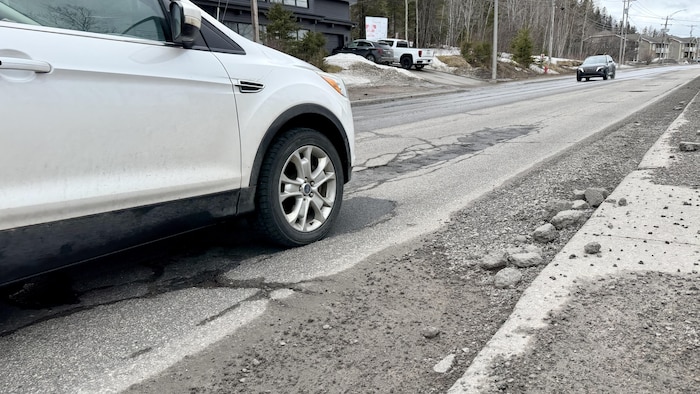 Une voiture circule sur une route asphaltée en mauvais état.