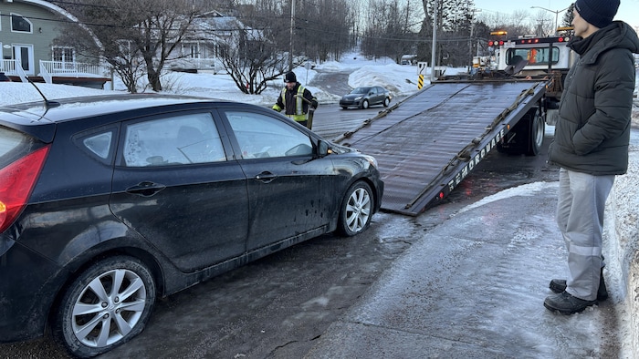 Un homme regarde une voiture avec deux crevaisons se faire remorquer.