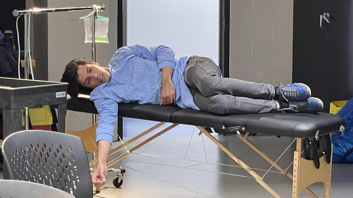 Un comédien est allongé sur une table qui se veut un lit d'hôpital.