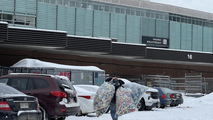 Une personne porte des sacs remplis de canettes et de bouteilles.