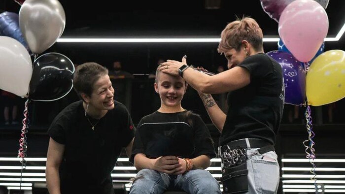 Une coiffeuse rase la tête d'une jeune fille au centre d'un ring de boxe.
