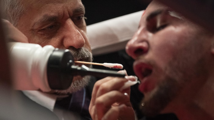 Un homme de coin tient un coton-tige ensanglanté près de la bouche d'un boxeur en pause pendant un combat.