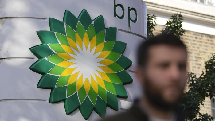 Un homme marche devant une affiche montrant le logo de la pétrolière BP.