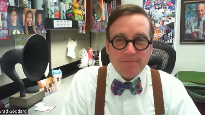 Brad Goddard est assis dans un bureau, arborant un nœud papillon coloré, des lunettes et des bretelles au-dessus de sa chemise.