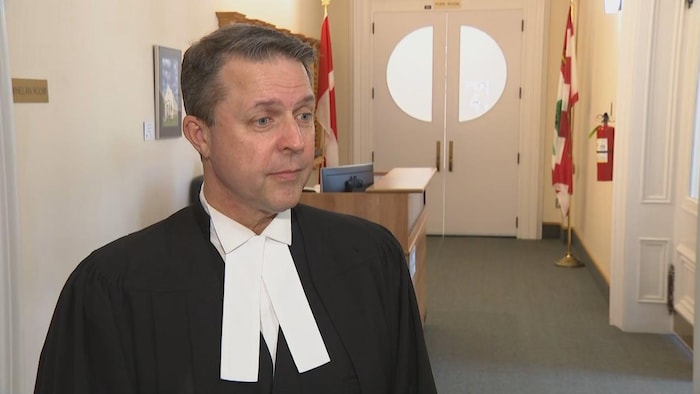 Brad Trivers dans un couloir, vêtu des habits officiels du président de la Chambre.