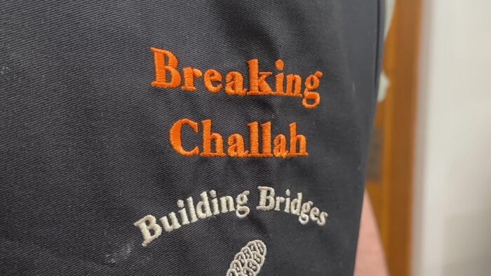 Les mots Breaking Challah en orange et Building Bridges en blanc, tissés sur un tissu noir.