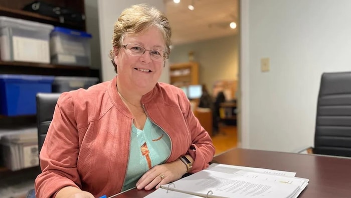Une dame assise à un bureau, avec un document devant elle.