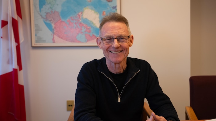 Brendan Hanley dans un bureau devant un drapeau canadien et une carte de l'Arctique.