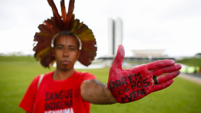 Un manifestant indigène contre l'ouverture des forêts pour l'exploitation minière au Brésil. Le manifestant a écrit sur sa main : « Cessez de nous tuer. »