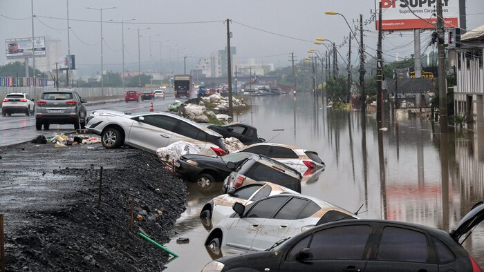 Des voitures abandonnées sont partiellement submergées sur le bord d'une route.