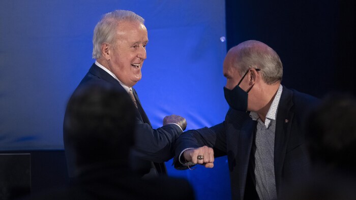 Brian Mulroney saluda con el codo a Erin O'Toole, que lleva una máscara.
