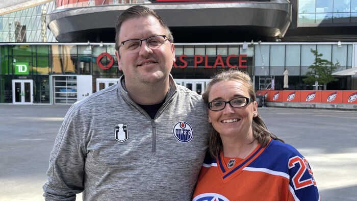Un couple avec des produits à l'effigie des Oilers d'Edmonton sourit à la caméra.