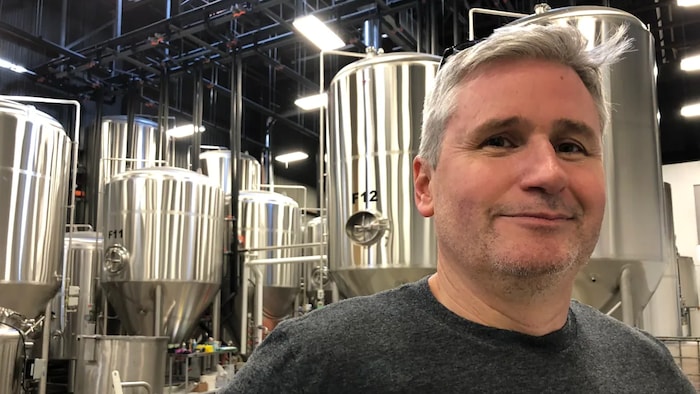 Un homme devant plusieurs cuves chromées où se fait le brassage de la bière.