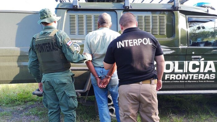 Un agent d'Interpol et un agent des services frontaliers du Costa Rica derrière un homme menotté.