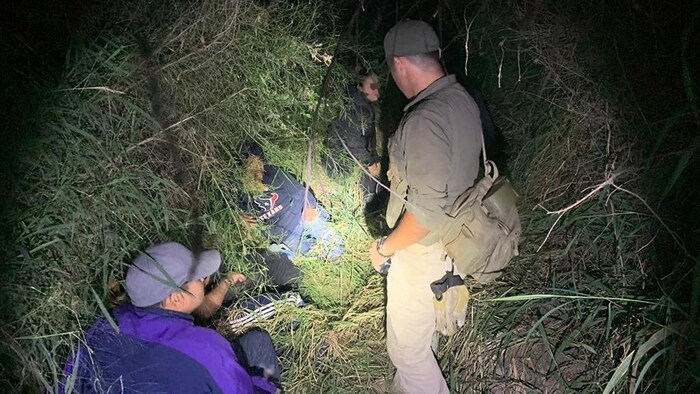 Un policier braque sa lampe de poche sur des gens cachés dans des broussailles.