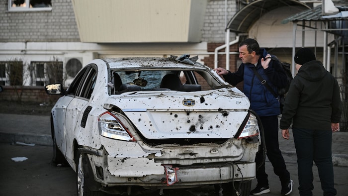 Deux personnes examinent un véhicule endommagé devant un immeuble résidentiel.
