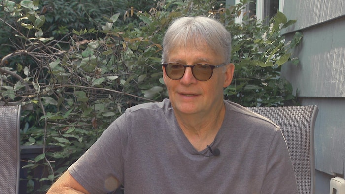 Un homme assis sur une chaise de patio en été devant un arbre.