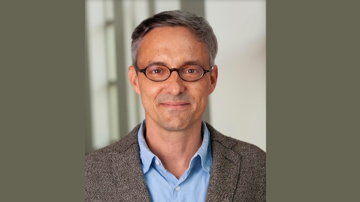 Professeur portant lunette et veston regardant l'objectif en souriant