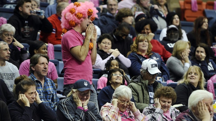 Un homme, debout parmi la foule dans un aréna, chante à tue-tête.