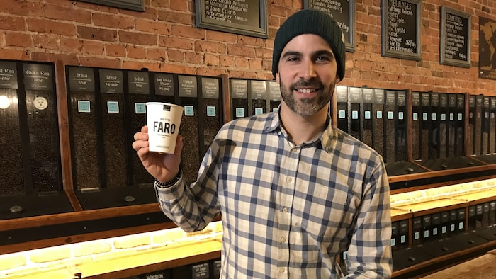 Maxime Fabi sourit pour la photo en tenant un gobelet de café dans ses mains.