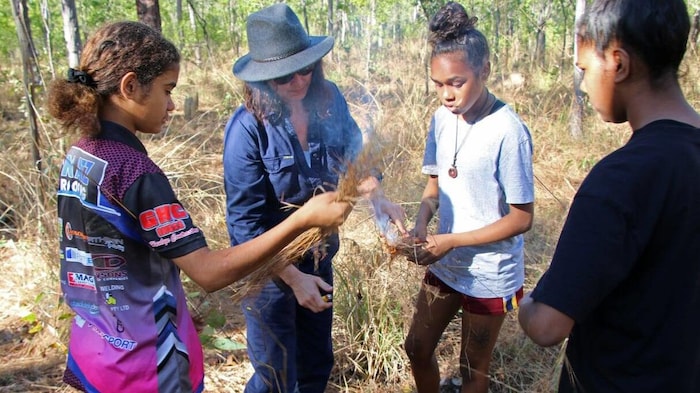 Trois jeunes Aborigènes et une femme blanche sont regroupés pour une activité.