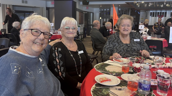 Trois dames âgées sont assises à une table pour manger.