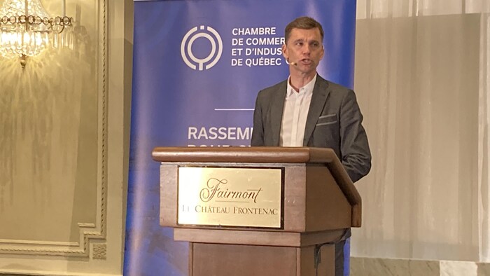 Le maire de Québec parle devant un podium devant la Chambre de commerce et d'Industrie de Québec.