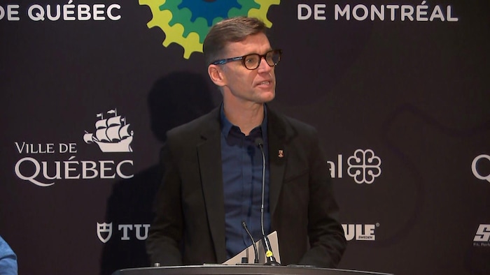 Un homme parle au micro lors d'une conférence de presse. 