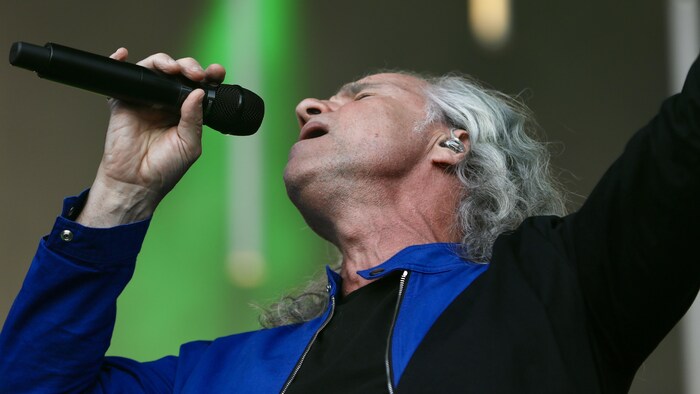 Le chanteur chante, les yeux fermés, un bras vers le ciel.