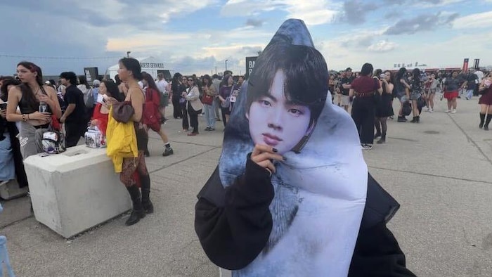 Une fan se couvre le visage d'un masque à l'effigie de Kim Seok-jin, membre du groupe BTS, plus connu sous le nom de « Jin », à Toronto, le samedi 22 août 2026.