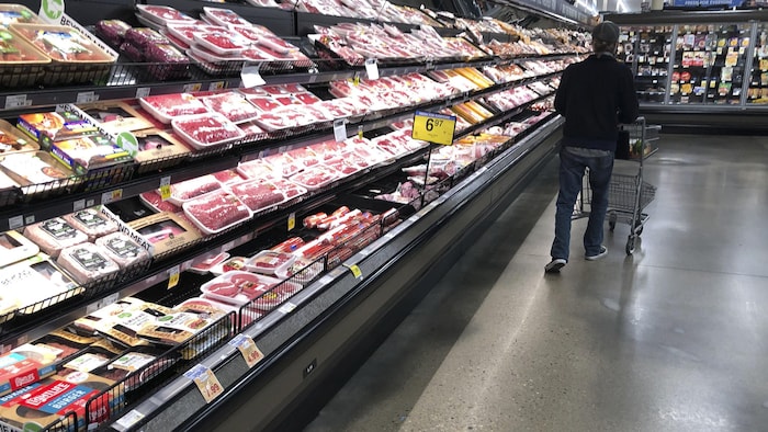 Un homme marche sans s'arrêter devant la section des viandes, à l'épicerie.