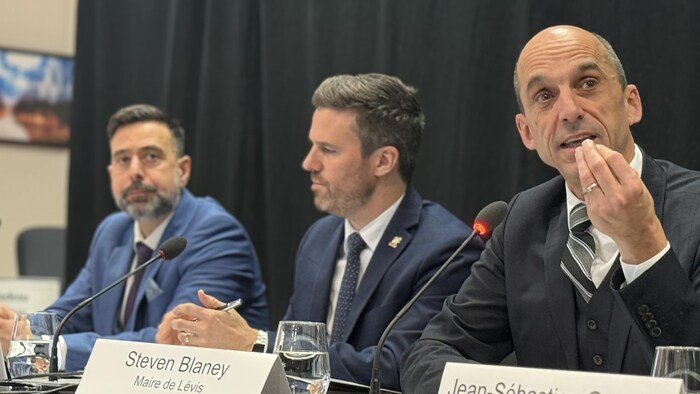 Le maire Steven Blaney assis derrière un micro en compagnie du directeur général et du directeur des finances de la Ville de Lévis.