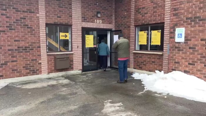Deux hommes entrent dans un bureau de vote à Sudbury. L'un d'eux se frotte les mains pour les réchauffer.