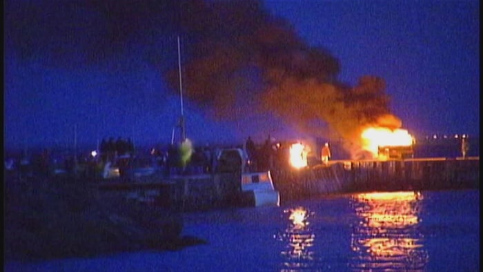 Un bateau en feu sur un quai, le soir. Image d'archive de mauvaise qualité.