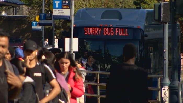 Des personnes attendent l'autobus alors qu'un autobus affiche un message disant qu'il est plein.