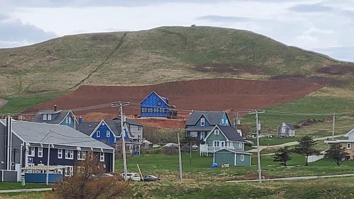 Une maison en construction en contrebas d'une butte avec un vaste pan de terrain qui a été nivelé.