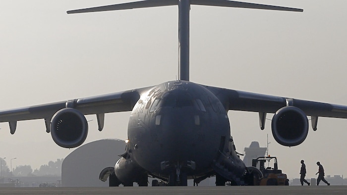 Deux militaires marchent vers un avion, photographié de face. 