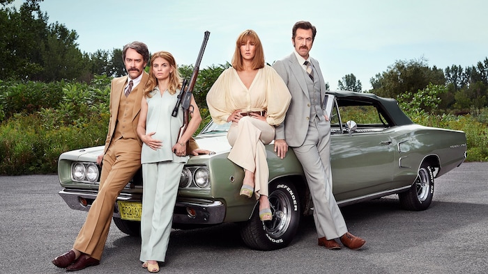 Les acteurs et actrices posent habillés et coiffés comme dans les années 1970 devant une voiture d'époque. 
