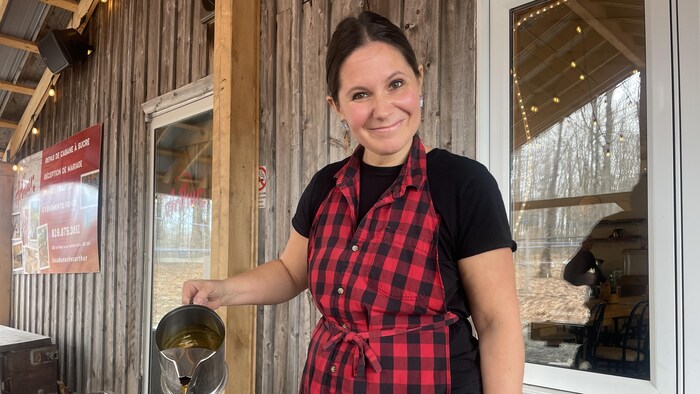 La propriétaire sourit à la caméra en versant de la tire d'érable sur de la neige.