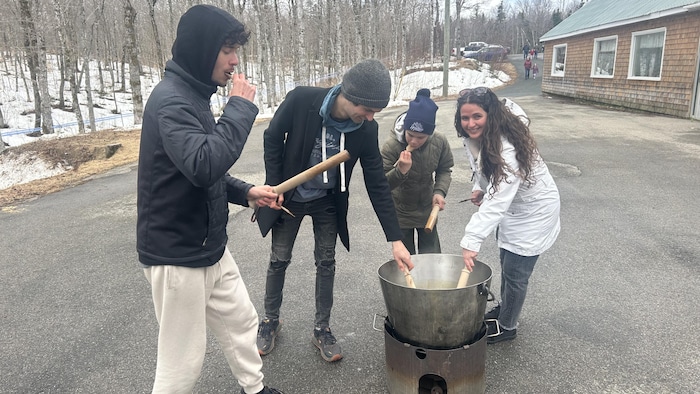 Quatre personnes dehors plongent des bâtons dans une cuve.