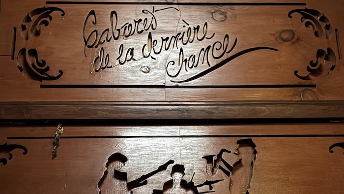 Les mots «Cabaret de la dernière chance» gravés dans le bois avec style, au-dessus de trois musiciens, un guitariste, un joueur de batterie et un saxophoniste, aussi taillés dans le bois.
