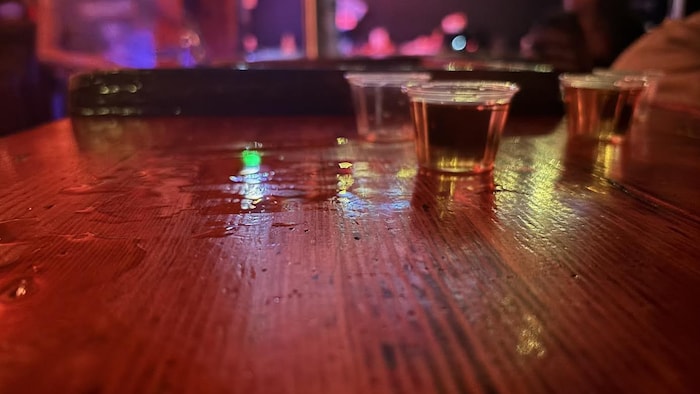 Deux petits verres remplis d'alcool sur un comptoir en bois.