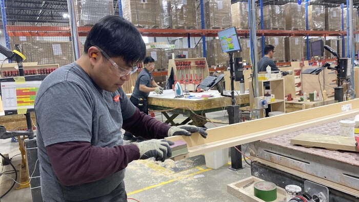 Un homme travaille avec son équipement de protection. D'autres employés travaillent autour.