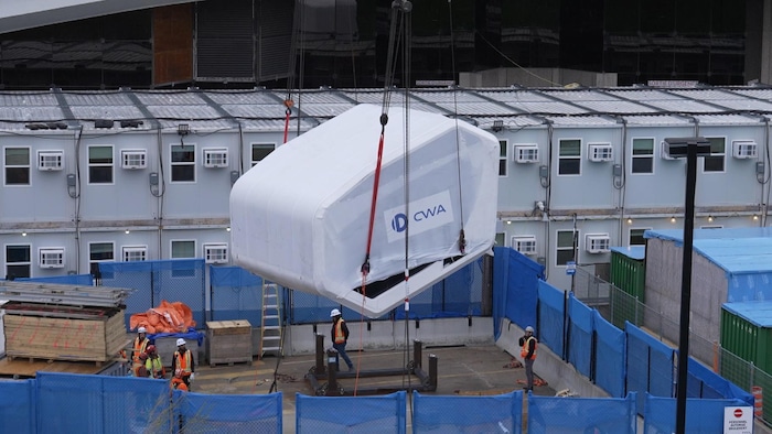 La cabine avec son protecteur, hissée sur des câbles au-dessus du chantier.