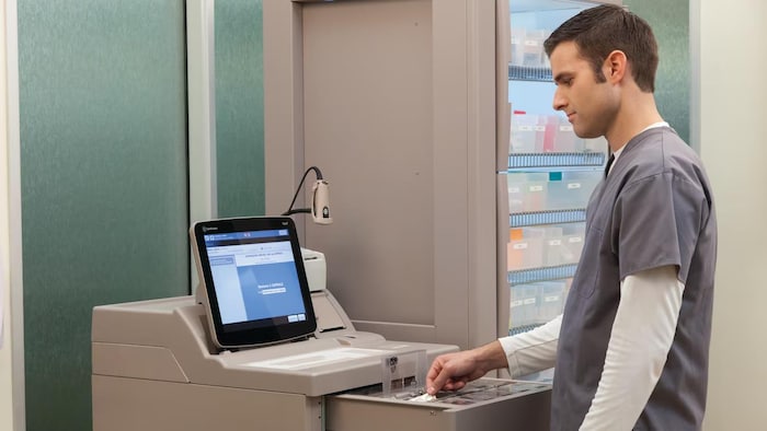 Un professionnel de la santé récupère un médicament dans un distributeur de médicament fonctionnant à l’aide d’un logiciel et d’un écran tactile.