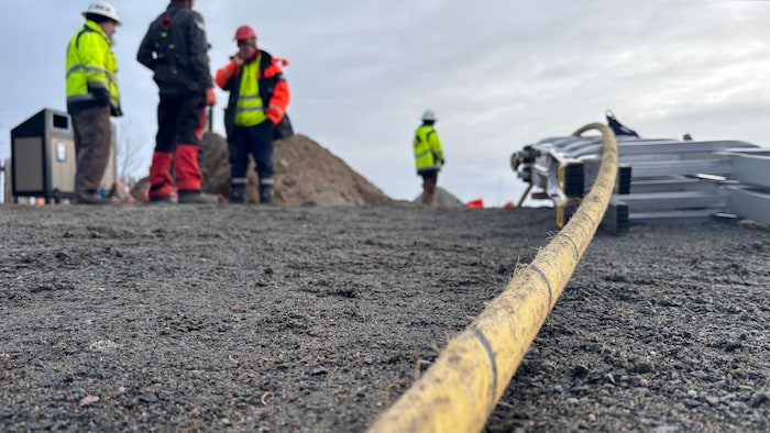 Un câble de fibre optique sur de la terre avec des travailleurs plus loin.