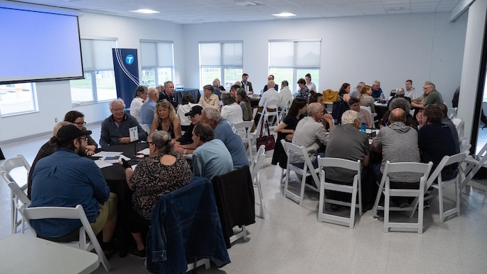Une quarantaine de personnes sont installées autour de tables rondes et échangent. 