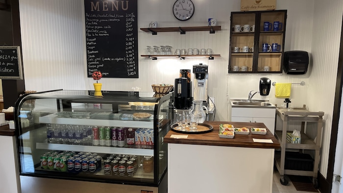 Un comptoir avec une machine à café, de la vaisselle et un réfrigérateur vitré présentant des boissons.